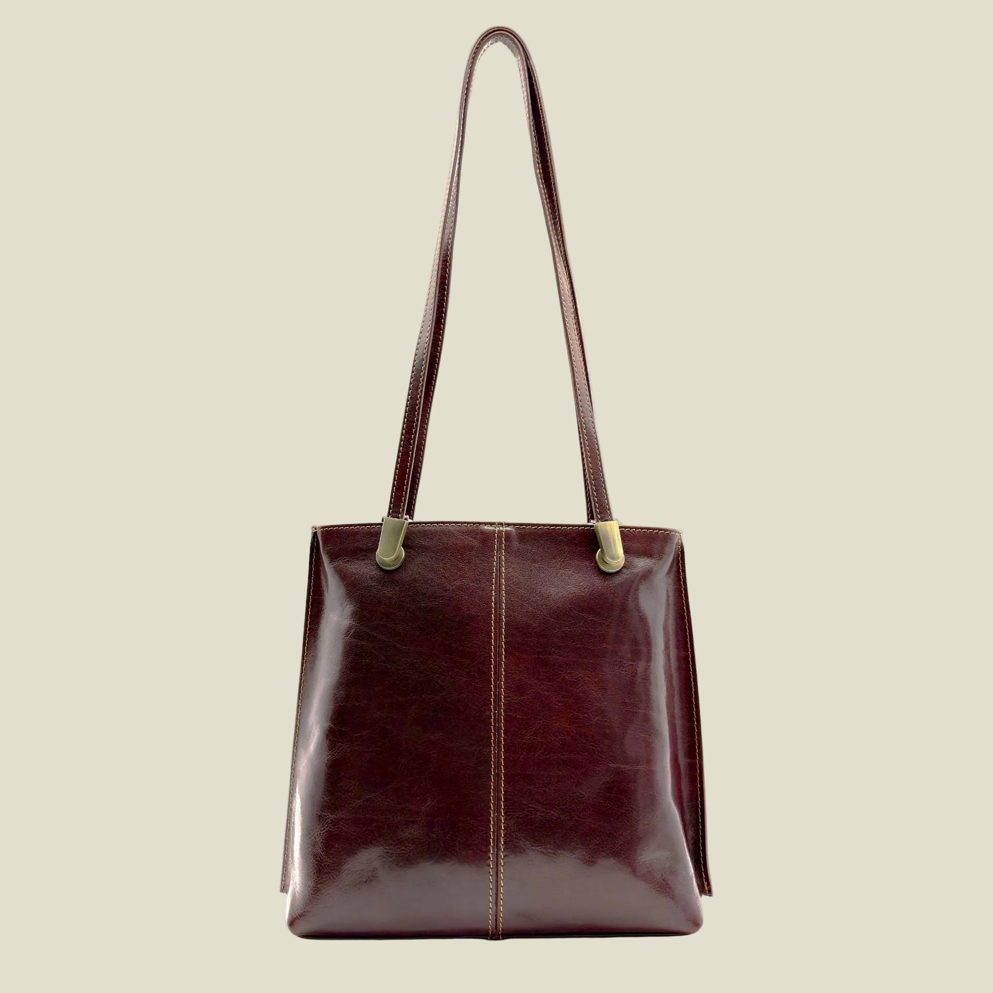 A dark burgundy leather tote bag with a glossy finish, featuring a central vertical seam, brass-tone hardware, and a single shoulder strap, shown against a plain white background.