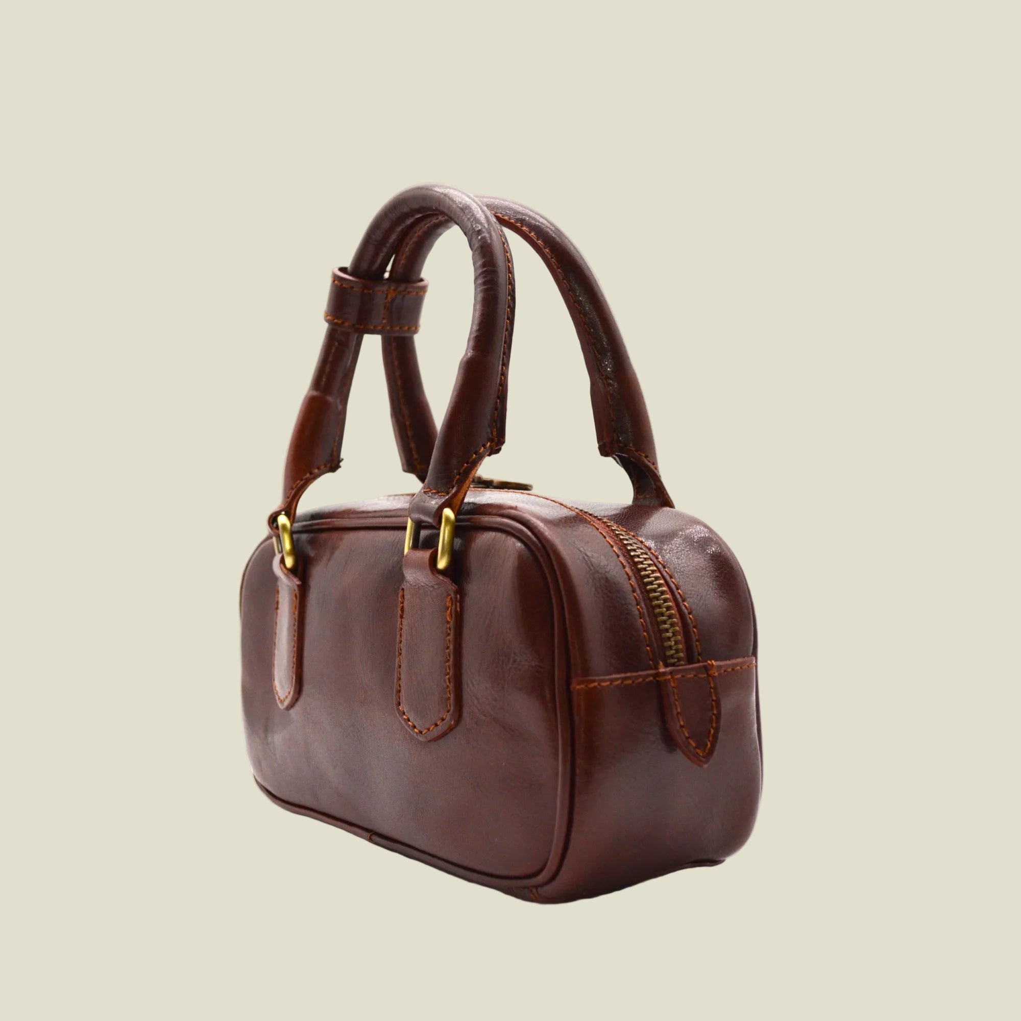 A brown leather handbag with double top handles, gold-tone hardware, and a zippered top closure, photographed on a clean white background.