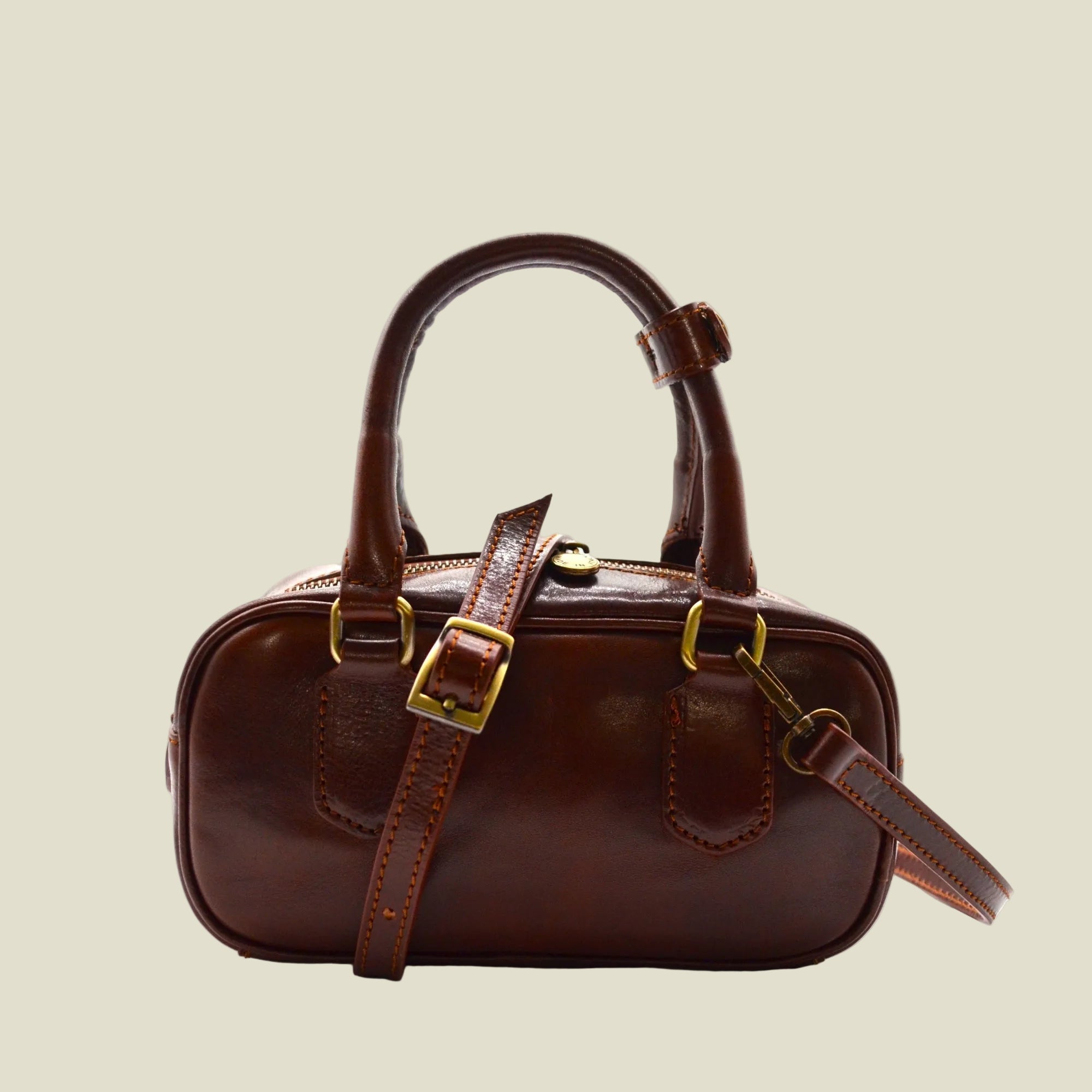 A dark brown leather handbag with gold-tone hardware, featuring dual top handles, a detachable shoulder strap, and a zippered closure, set against a plain white background.