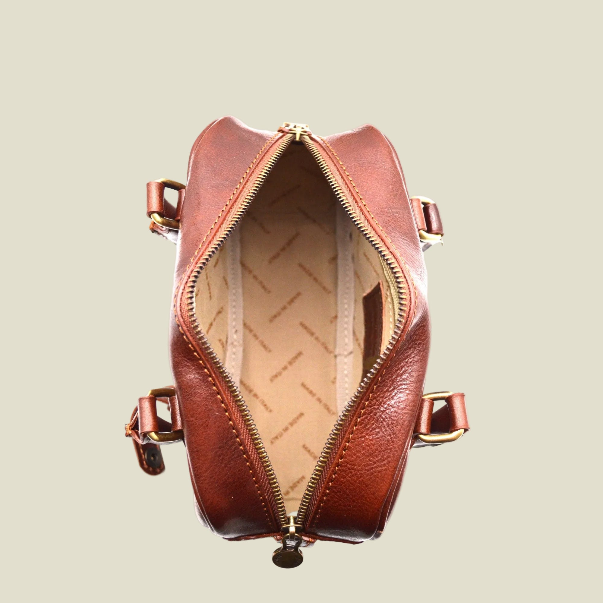 A brown leather handbag shown open from a top-down view, revealing a beige patterned interior lining and gold-tone hardware.