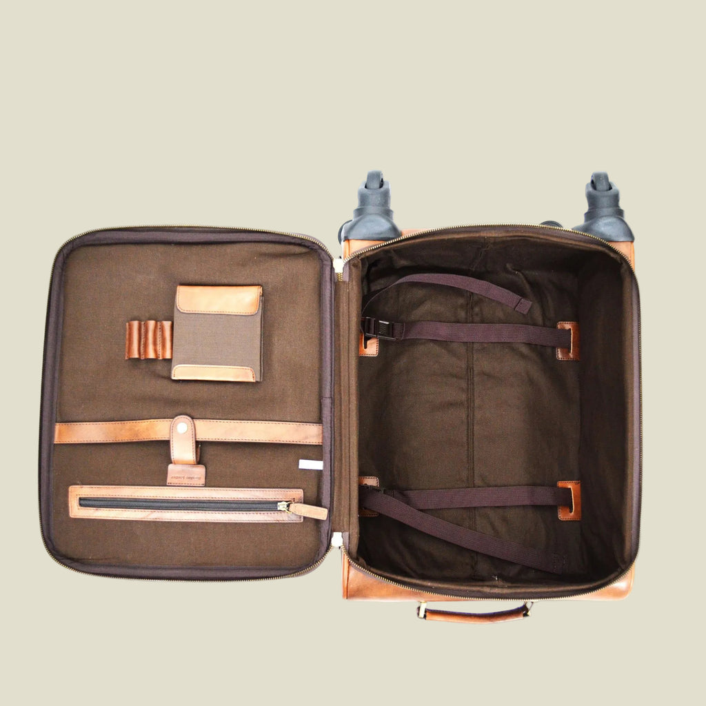 An open soft-sided suitcase or luggage compartment shown from above on a white background, revealing a dark brown interior with multiple zip compartments, straps, and a padded handle.
