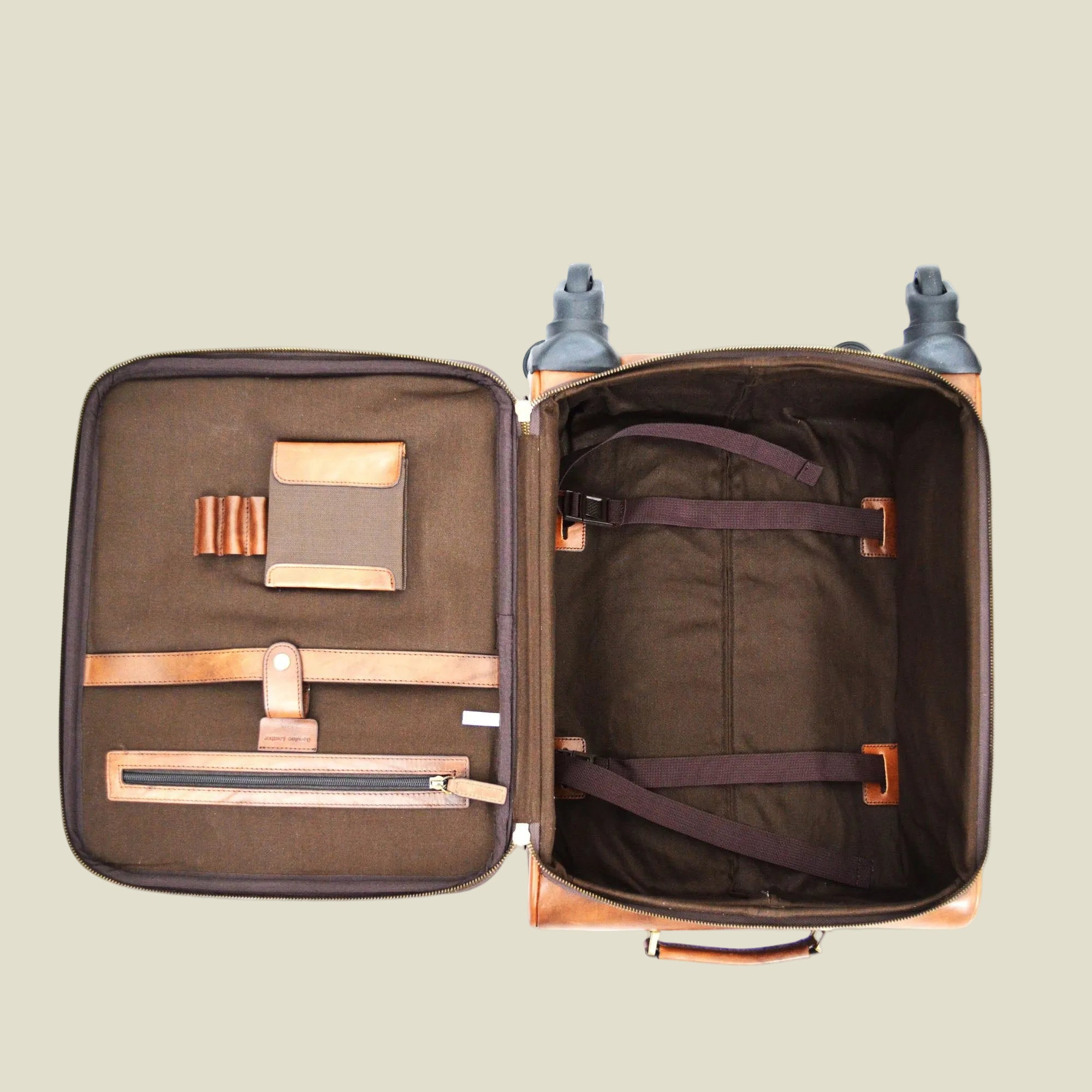 An open soft-sided suitcase or luggage compartment shown from above on a white background, revealing a dark brown interior with multiple zip compartments, straps, and a padded handle.