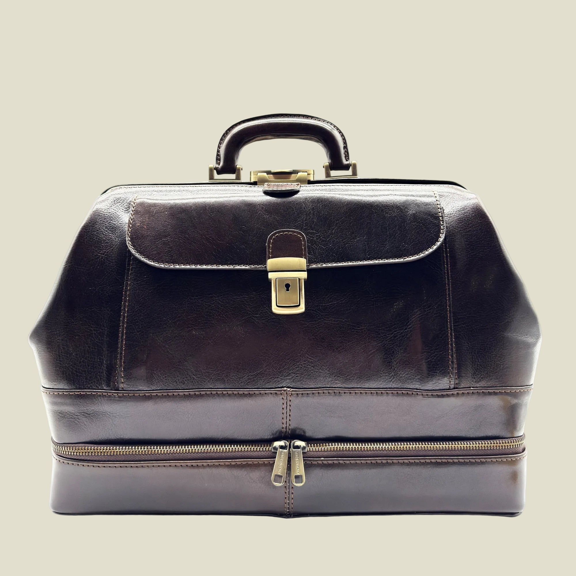 A dark brown leather doctor's bag or briefcase with a top handle, a front flap secured by a brass lock, and a lower zippered compartment, shown against a plain white background.