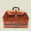 A brown leather doctor's bag or briefcase with a top handle, front flap pocket, brass-tone lock, and a zippered lower compartment, shown on a plain white background.