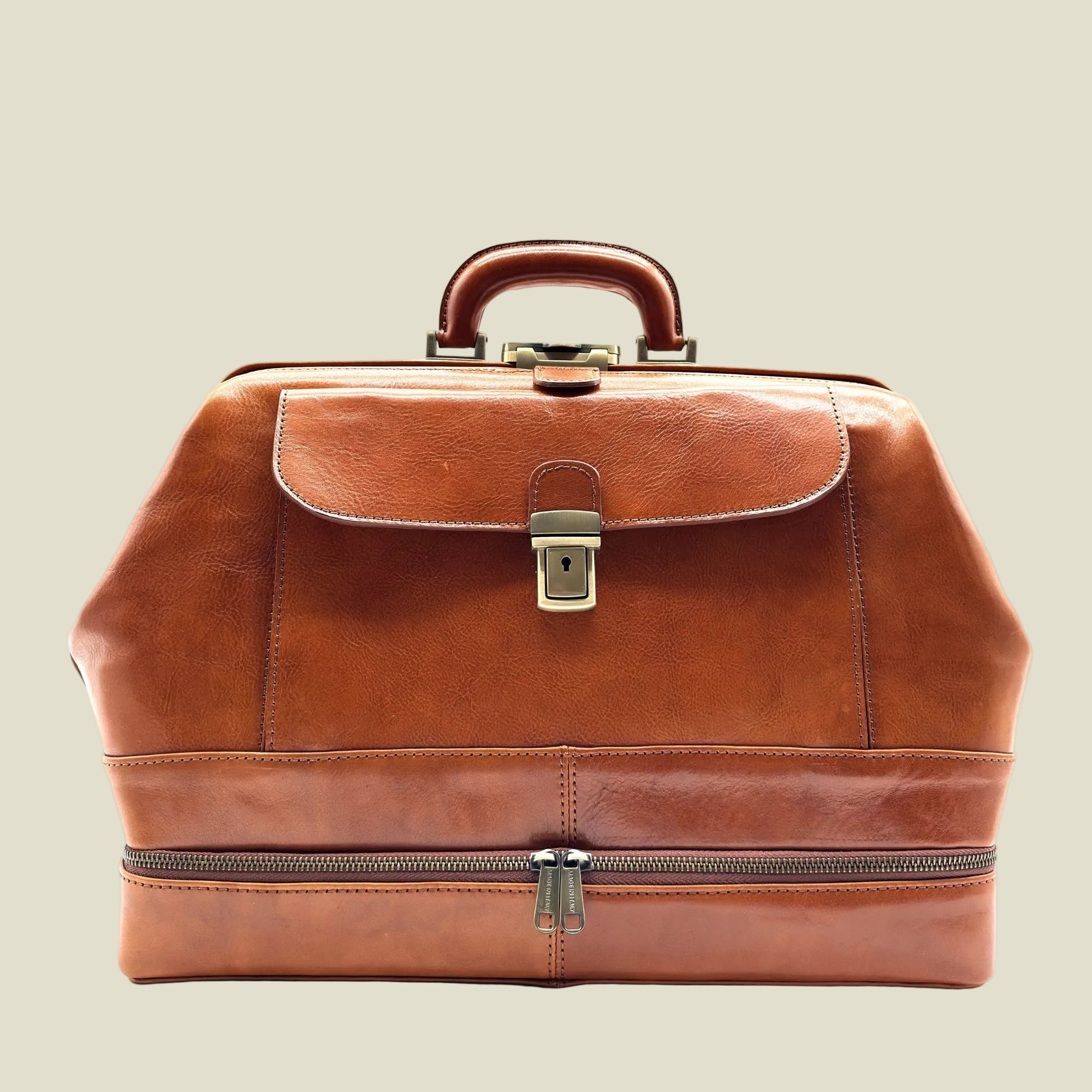 A brown leather doctor's bag or briefcase with a top handle, front flap pocket, brass-tone lock, and a zippered lower compartment, shown on a plain white background.