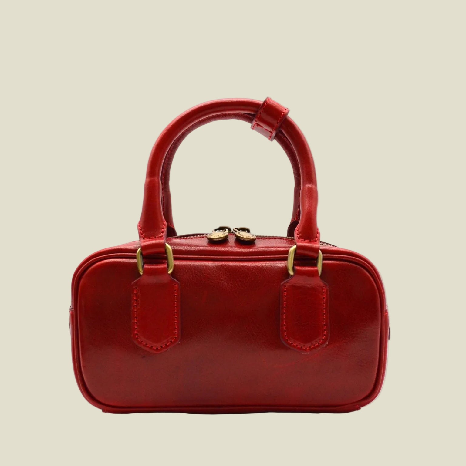 A small red leather handbag with a top handle, gold-tone hardware, and two front tab details, shown against a plain white background.