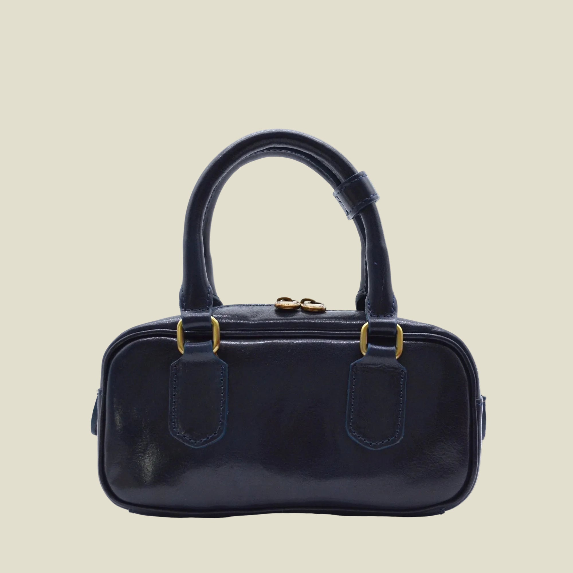 A small structured handbag in glossy dark navy leather with a top handle, gold-tone hardware, and matching navy stitching, photographed on a clean white background.