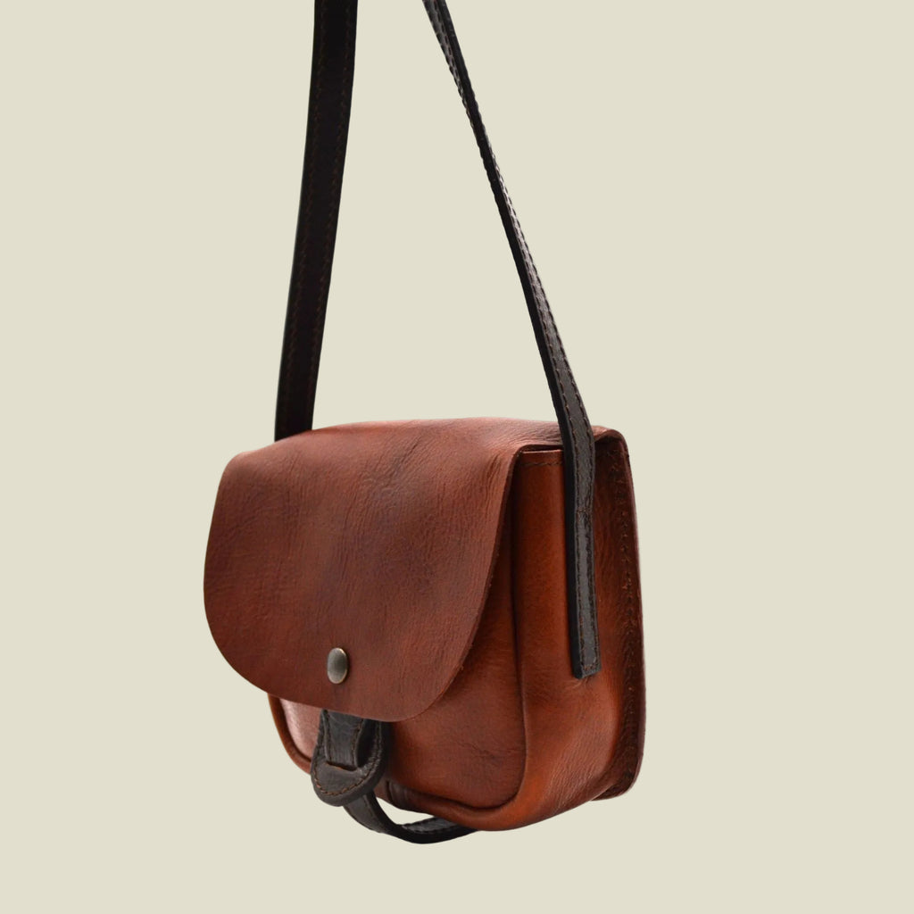 A brown leather crossbody bag with a curved front flap and a black shoulder strap, shown from a side profile on a white background.