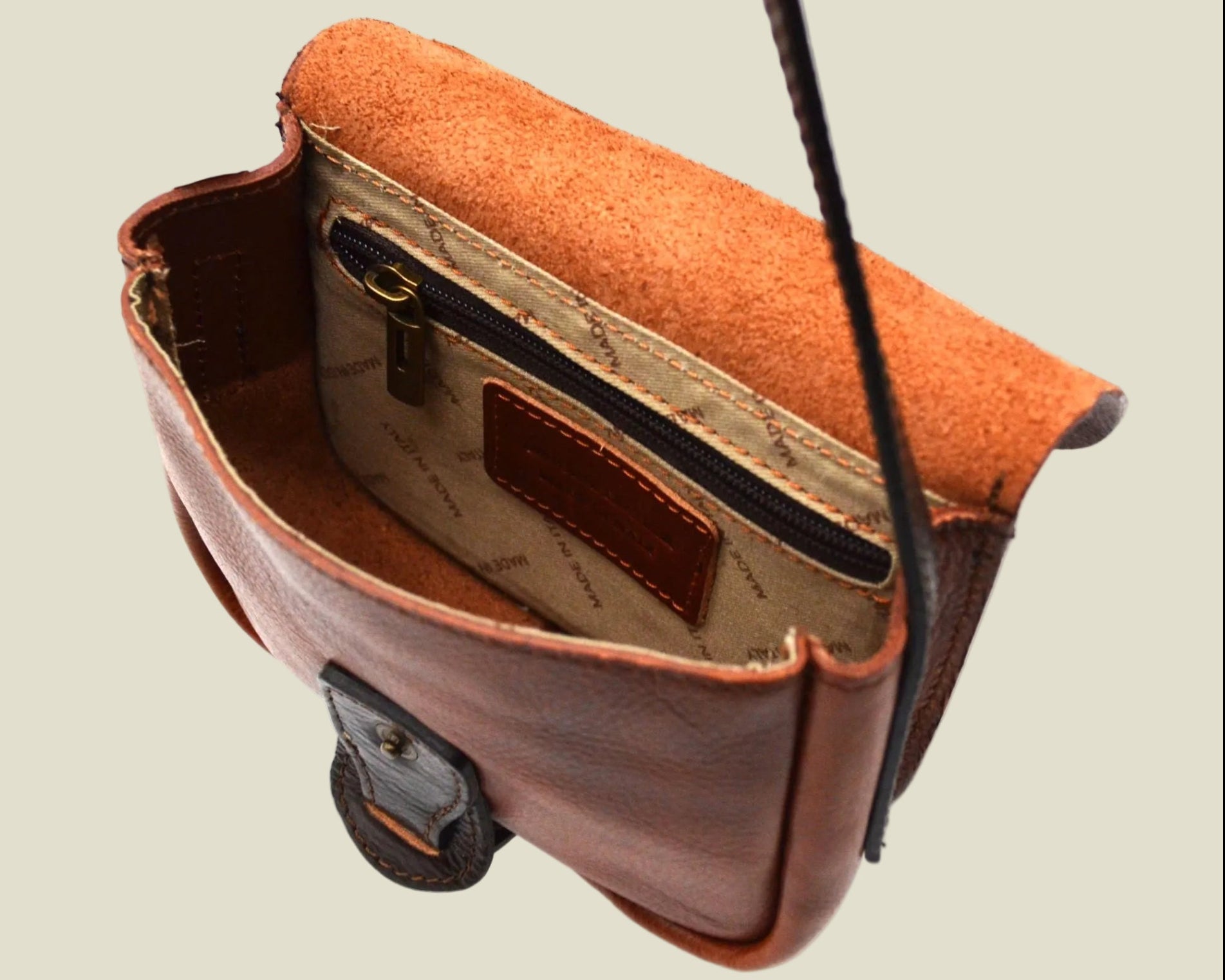 A brown leather crossbody bag with a warm orange-brown suede-like interior lining, shown open to display the zippered compartment and interior details against a white background.