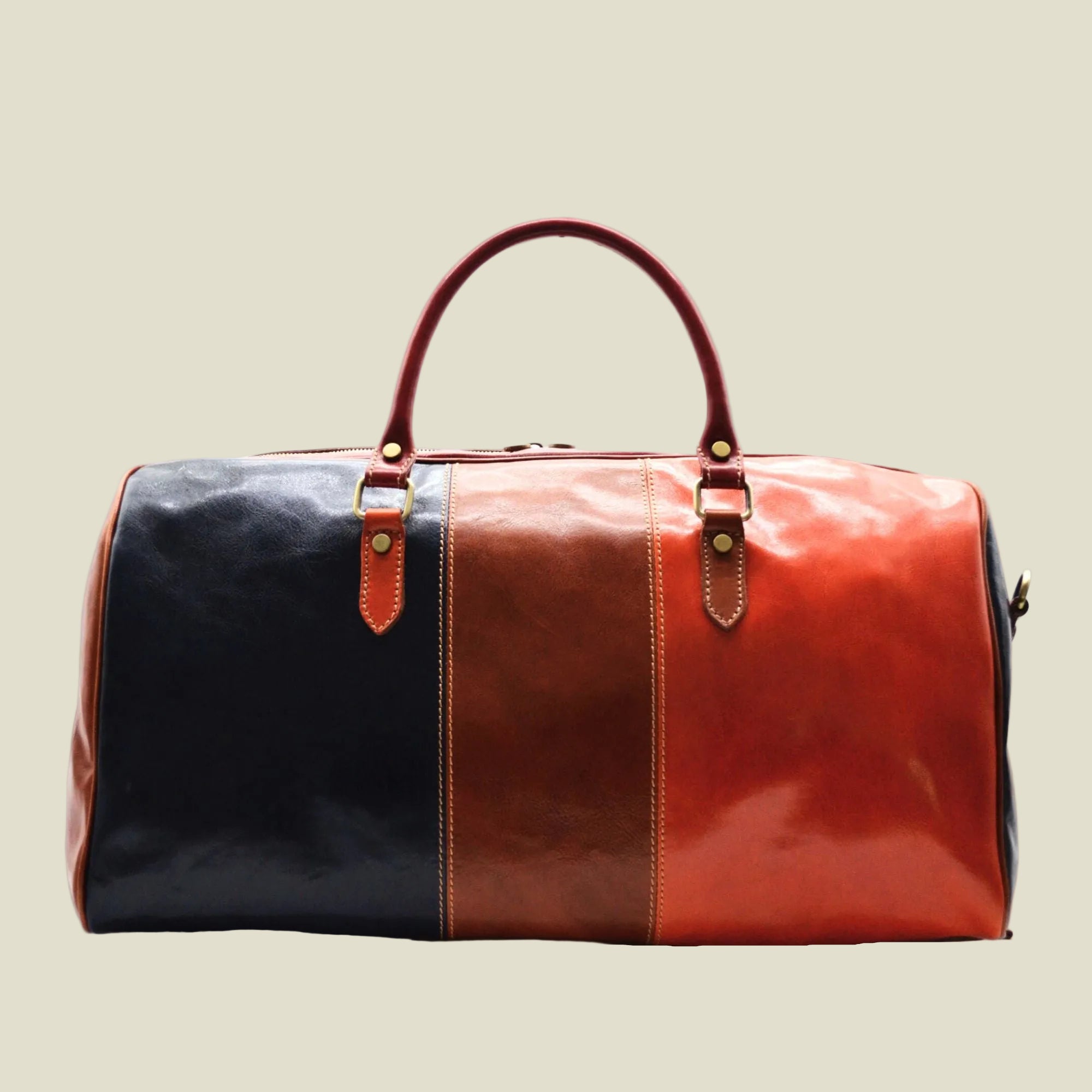 A leather duffel bag with a color-blocked design featuring a black left panel, a brown center panel, and a reddish-orange right panel, with matching brown leather handles and gold-tone hardware, shown against a plain white background.