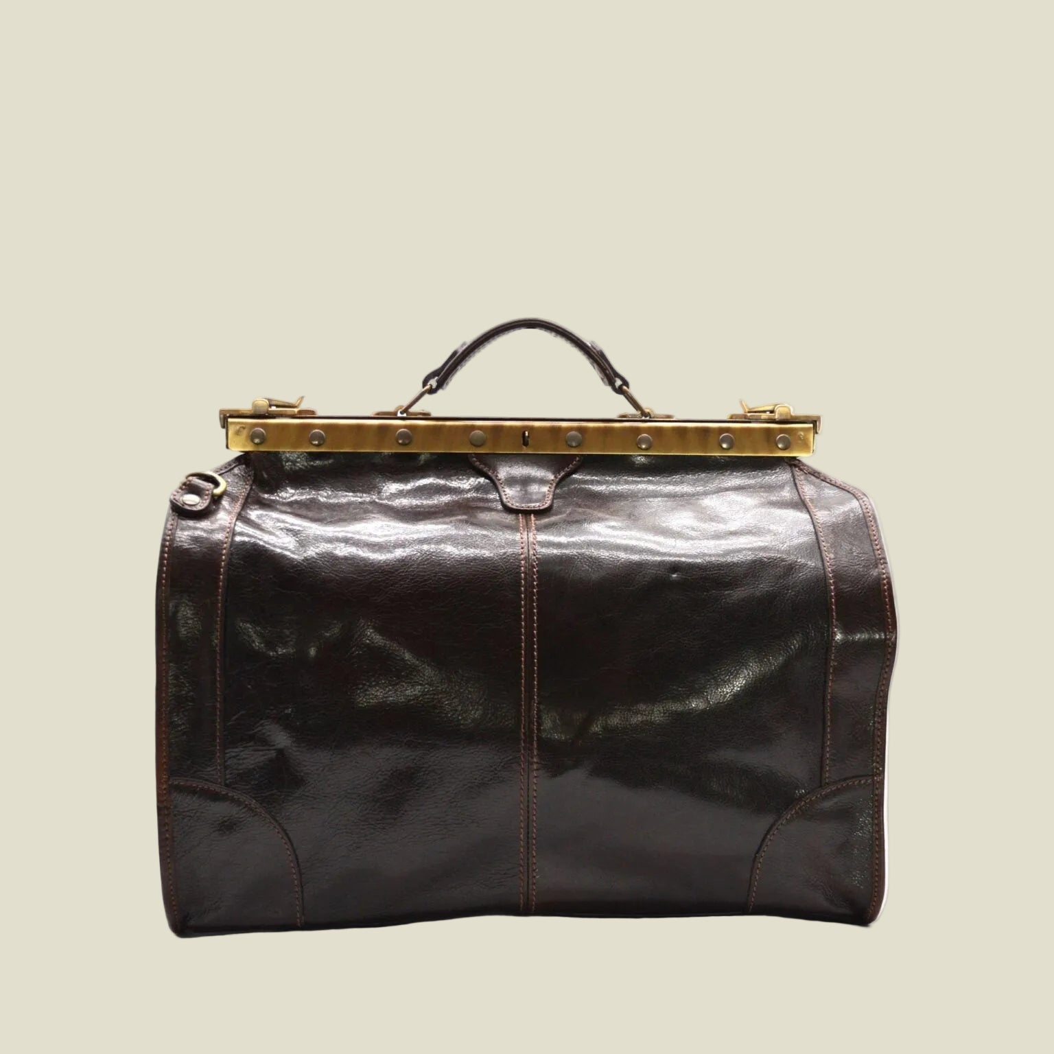 A dark brown leather duffel bag with a glossy finish, featuring a gold-toned metal frame clasp at the top and a black leather carry handle, shown against a plain white background.