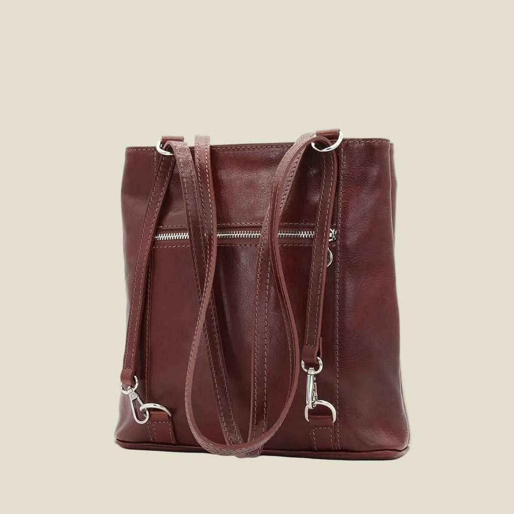 A dark brown leather tote bag with dual shoulder straps, a front zippered pocket, and silver-tone hardware, shown against a plain white background.