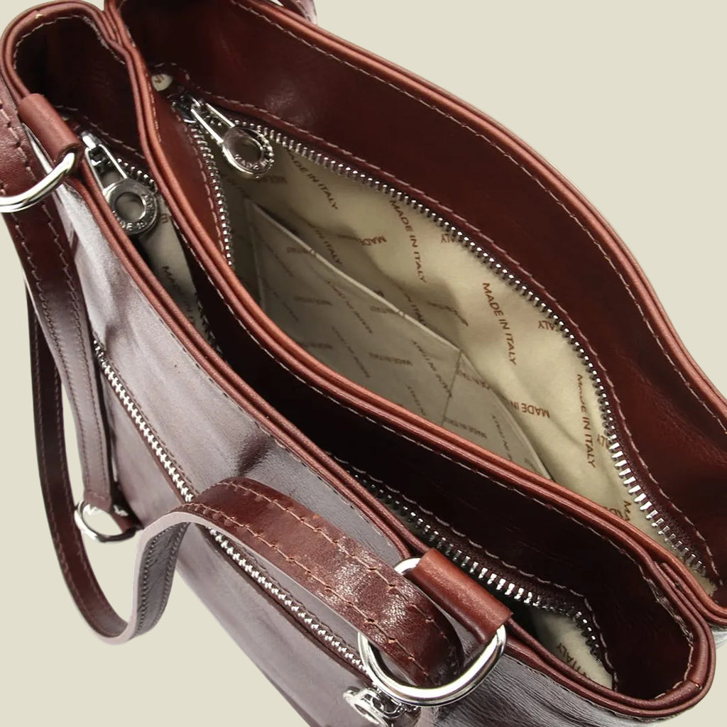 Close-up of a brown leather handbag showing the interior compartments, silver zippers, and a beige patterned lining.