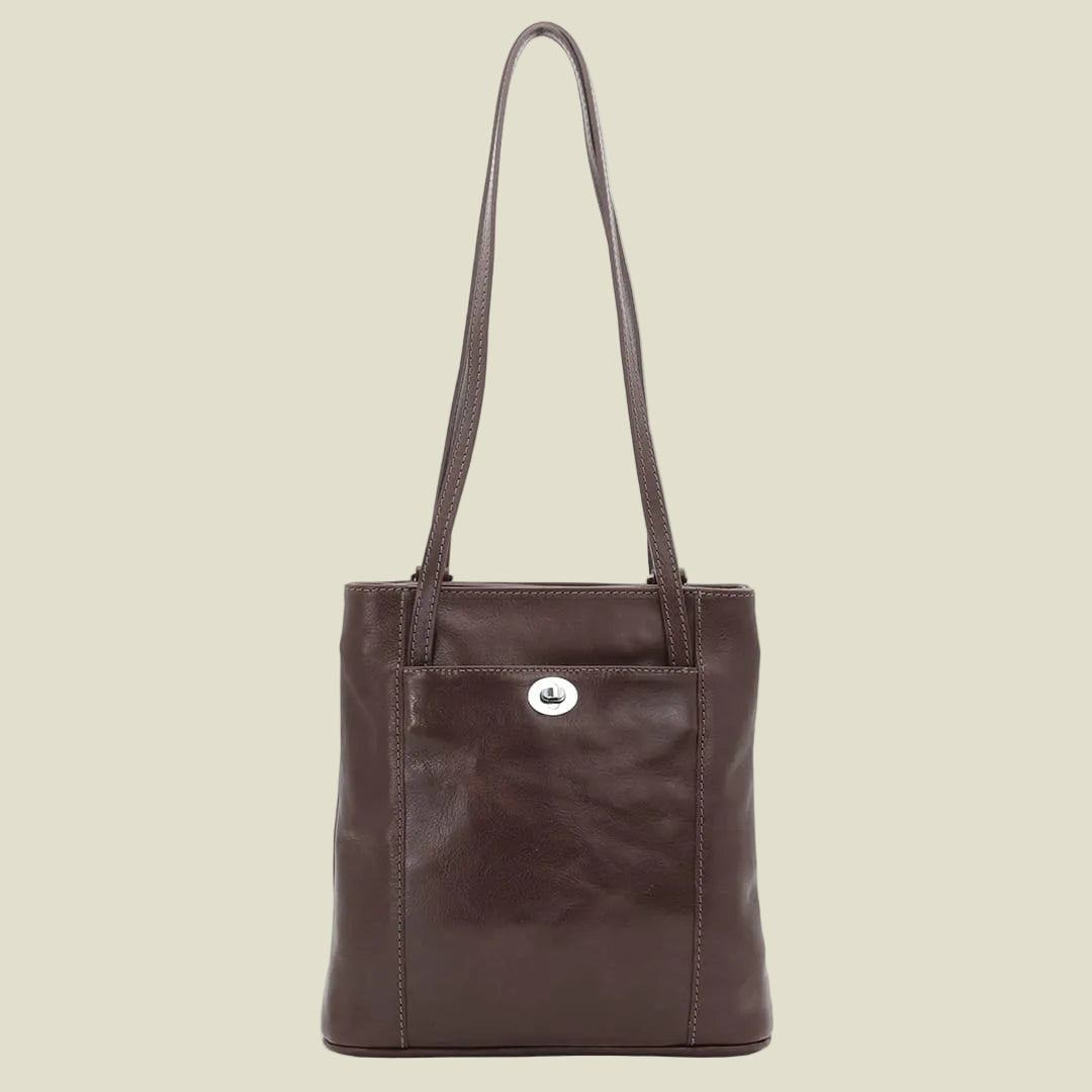 A dark brown leather tote bag with a single shoulder strap and a small silver-tone logo medallion on the front pocket, shown against a plain white background.