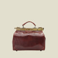 A vintage-style leather doctor's bag in reddish-brown with a gold-tone metal frame and handle, shown against a plain white background.
