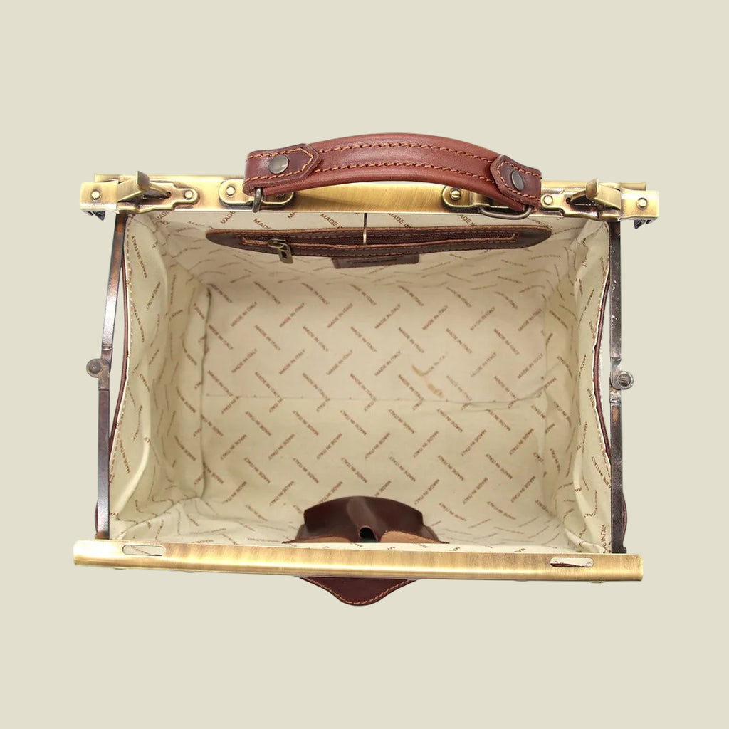 An open vintage-style hard case or suitcase with a tan leather handle, gold-toned metal hardware, and a cream patterned interior lining.