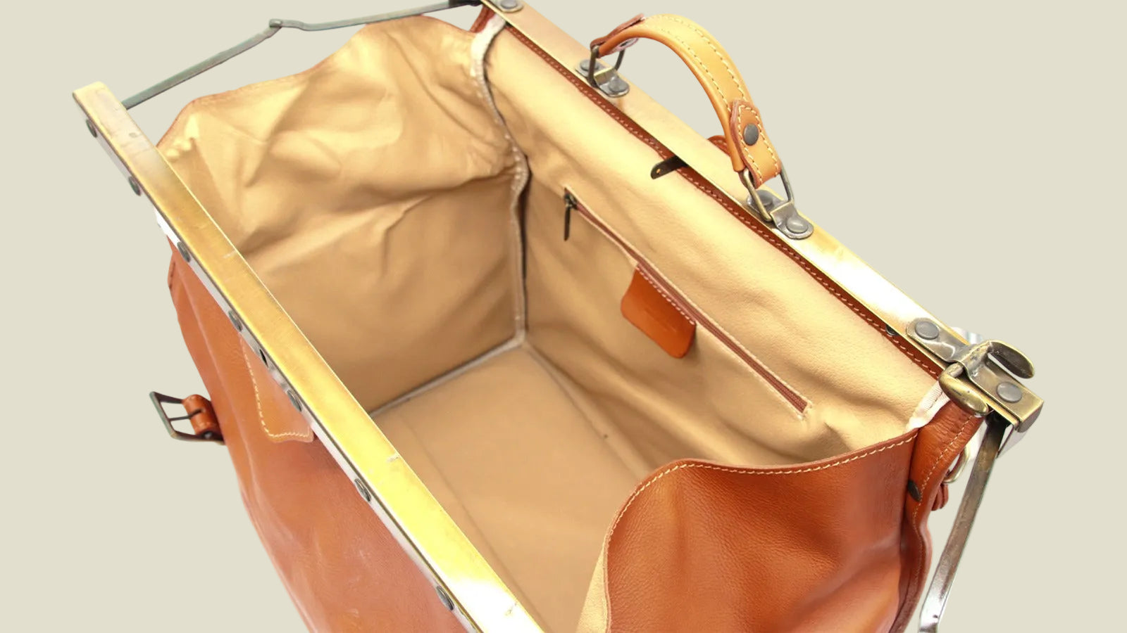A vintage leather satchel or briefcase shown open, featuring tan leather exterior, a beige fabric lining, and brass-tone metal hardware on a white background.