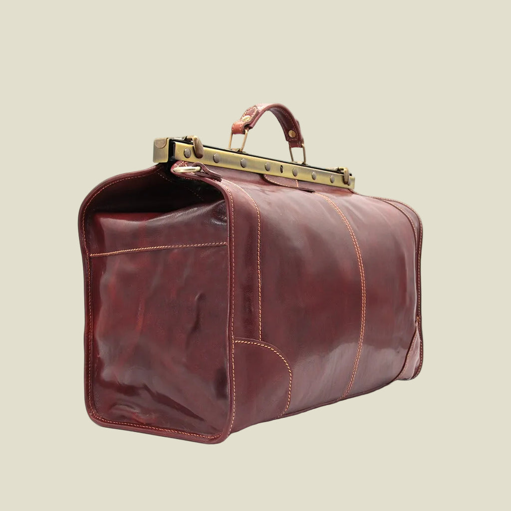 A dark reddish-brown leather duffel bag with gold-toned metal hardware and a top handle, shown on a plain white background.