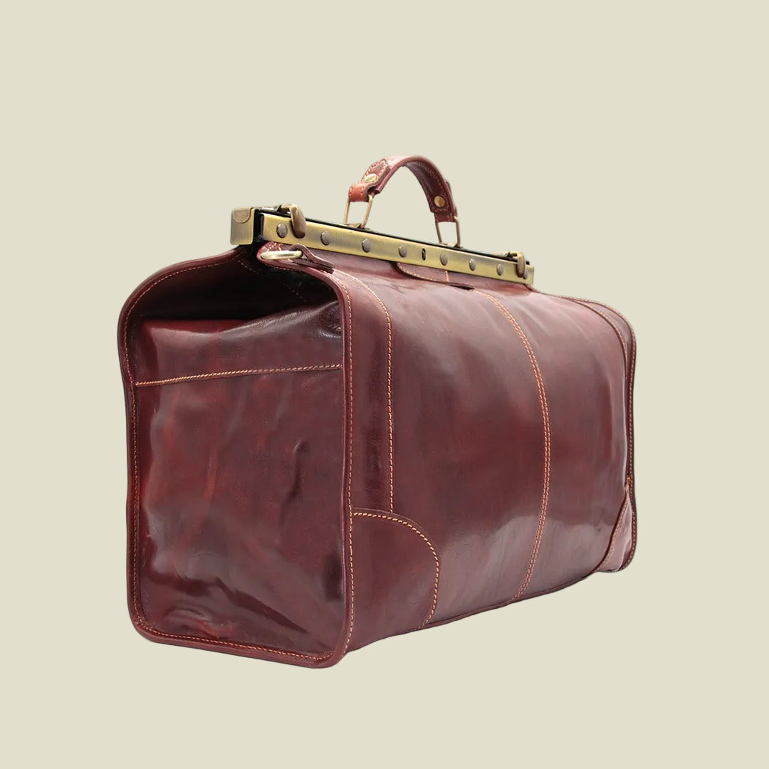 A dark reddish-brown leather duffel bag with gold-toned metal hardware and a top handle, shown on a plain white background.