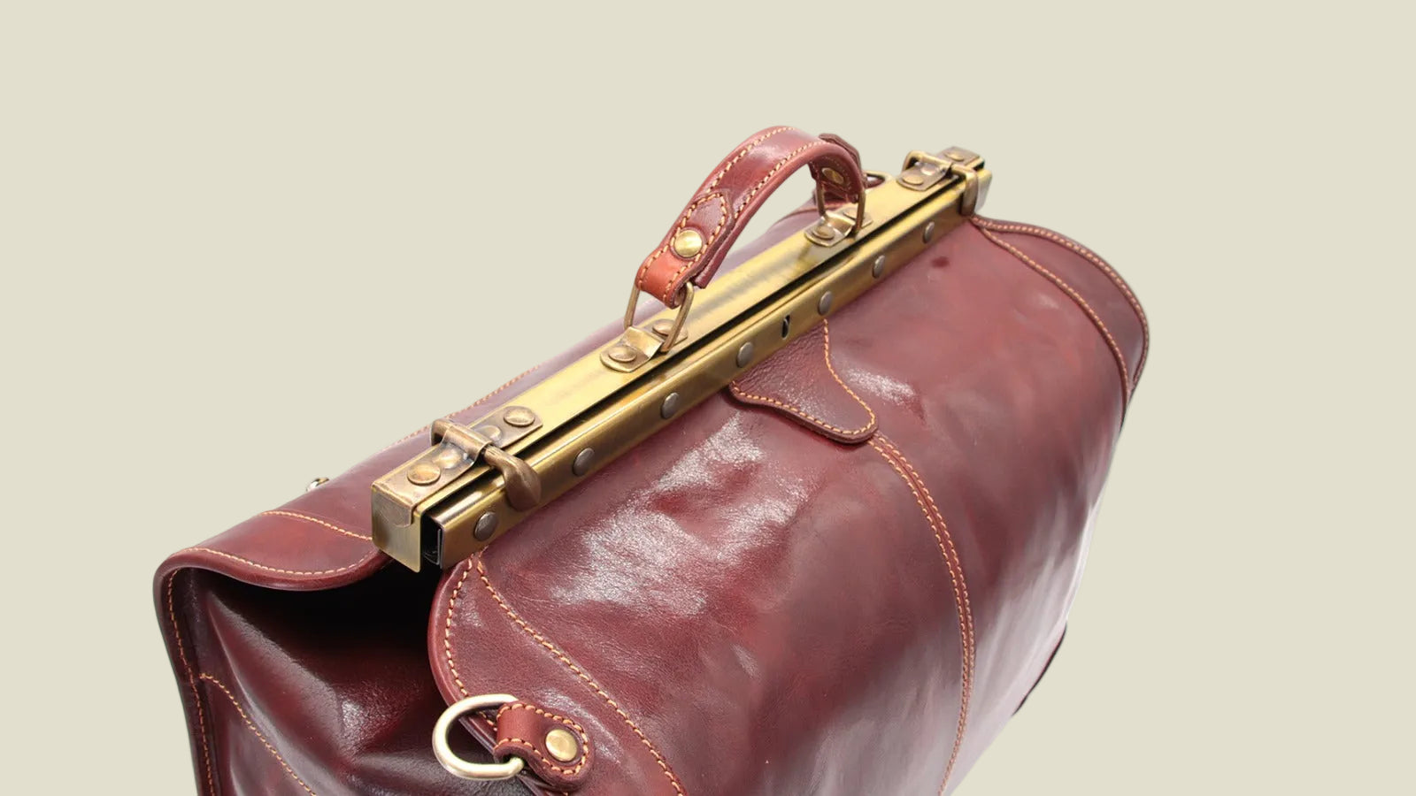A close-up of a dark reddish-brown leather satchel bag with a gold-tone metal clasp and handle, set against a plain white background.