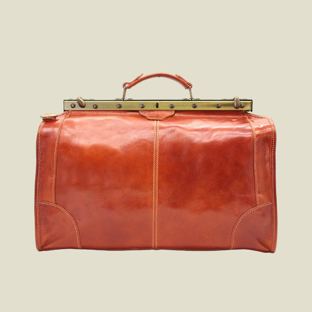 A classic leather duffel bag in a warm cognac brown, featuring a top handle, brass-tone hardware, and decorative stitching on a white background.
