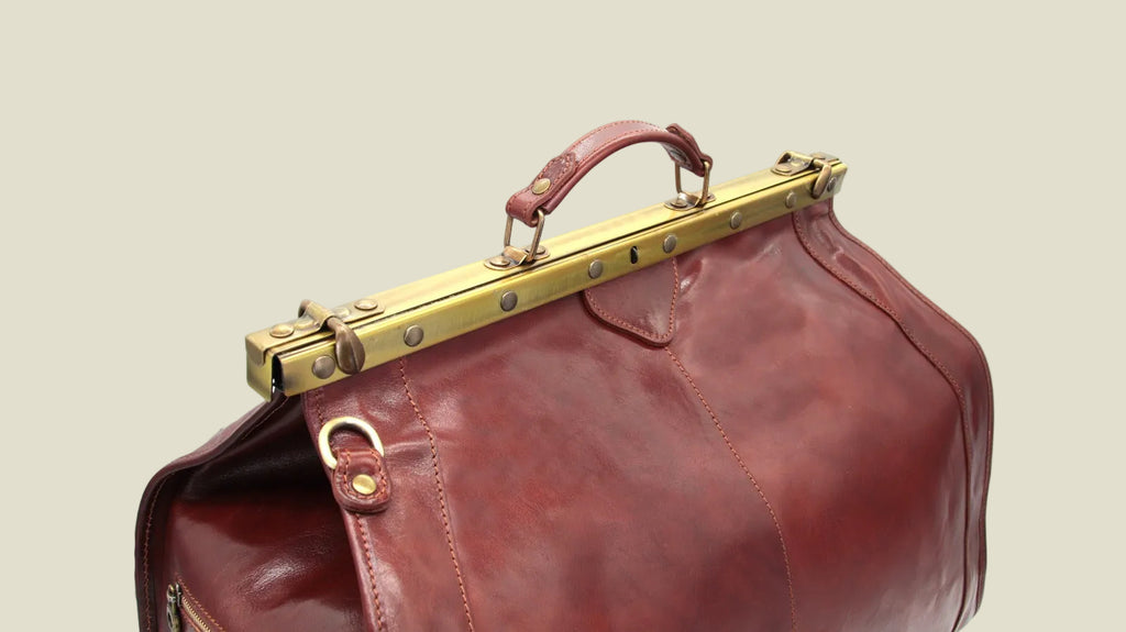 A close-up of a dark reddish-brown leather bag with a brass metal frame handle closure, shown against a plain white background.