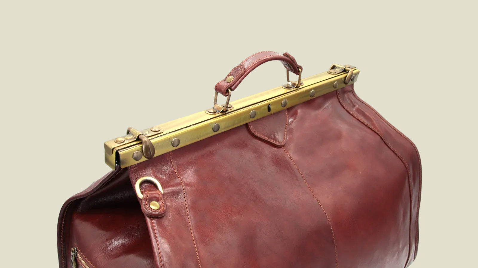 A close-up of a dark reddish-brown leather bag with a brass metal frame handle closure, shown against a plain white background.