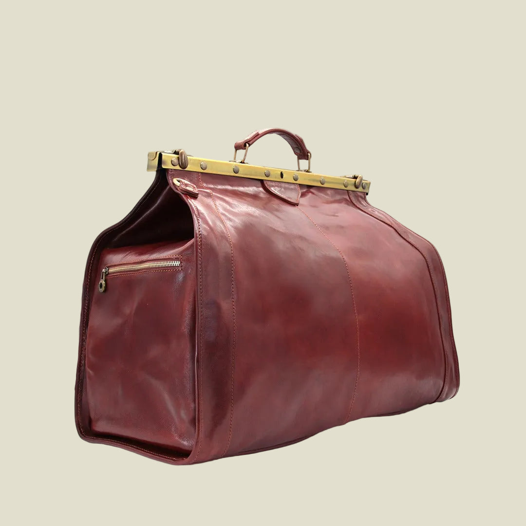 A burgundy leather duffel bag with a gold-tone metal frame handle and a zippered side pocket, shown on a white background.