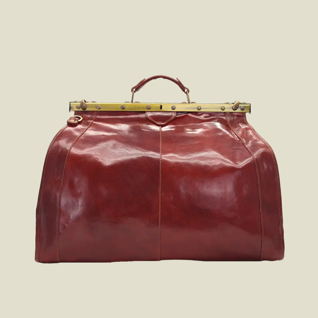 A large, glossy reddish-brown leather duffel bag with a top handle and a gold-tone metal frame clasp, shown against a plain white background.