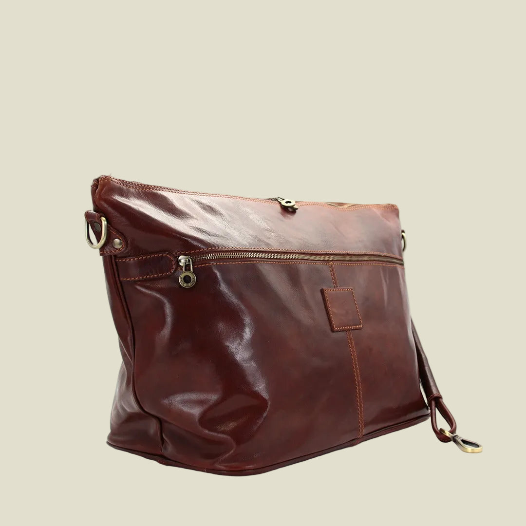 A brown leather shoulder bag with a top zipper, side zipper pocket, and a small leather patch on the front, photographed on a white background.