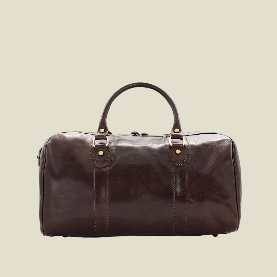 A dark brown leather duffel bag with double top handles, brass-tone hardware, and vertical stitched detailing, shown against a plain white background.