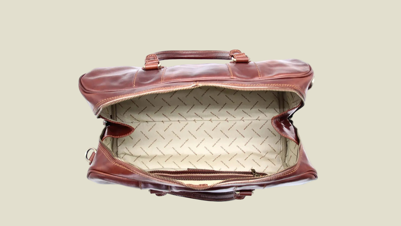 A brown leather duffel bag shown open from a top-down view, revealing a beige patterned interior lining and dark brown handles, set against a plain white background.