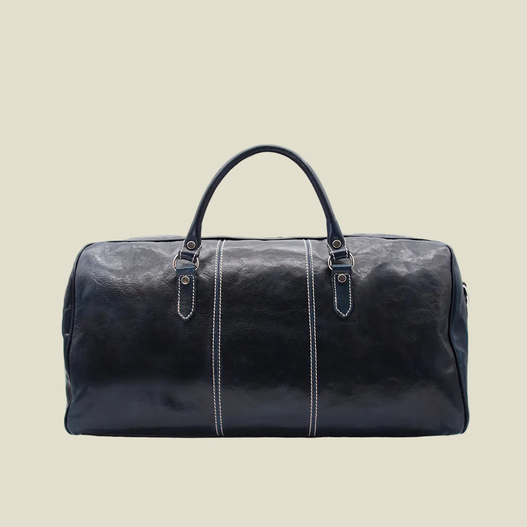 A dark navy blue leather duffel bag with a glossy finish, featuring dual top handles, vertical white contrast stitching, and gold-tone hardware on a white background.
