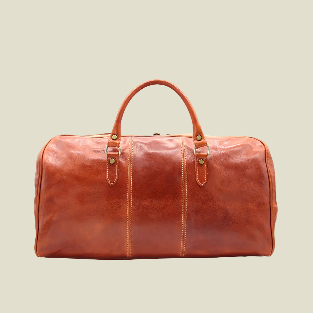 A brown leather duffel bag with dual top handles and brass-tone hardware, photographed against a plain white background.