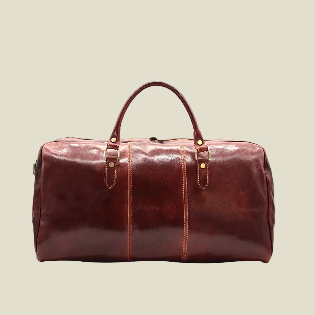 A dark reddish-brown leather duffel bag with double top handles, gold-tone hardware, and vertical contrast stitching, shown against a plain white background.