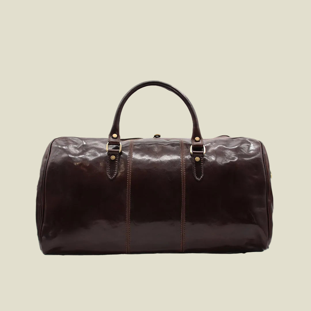 A dark brown glossy leather duffel bag with double top handles, brass-tone hardware, and vertical contrast stitching, shown against a plain white background.